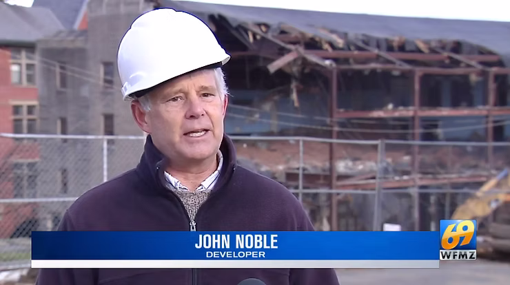 Owner John Noble wearing a white hard hat speaks during an on-site interview in front of a partially demolished building, with a “69 WFMZ” news banner displayed on screen.